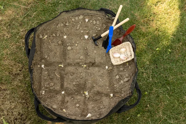 Miniature gardening tools placed over a grow bag. growing garlic in a grow bag