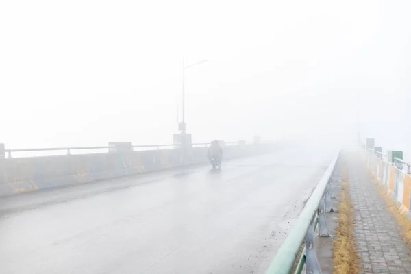 Motorcycles in dense fog crossing the bridge with low visibility