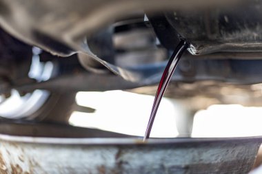 Changing engine dirty oil being drained from underneath a car into a tray clipart