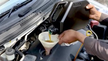 Tamirci arabanın motoruna yeni motor yağı döküyor.