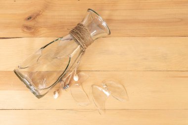 Ahşap bir masada şeffaf cam vazo kırılmış.