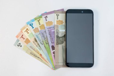 Beyaz arka planda izole edilmiş akıllı telefona sahip Suriye banknotları