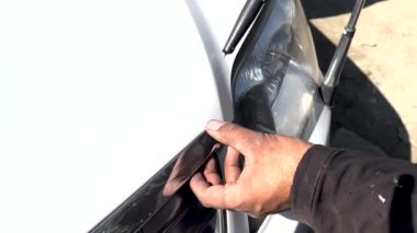 Araba atölyesindeki teknisyen parçayı onarmak için araba gövdesine yapışkan macun sürüyor.