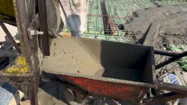 El arabasında beton karışımı var. İşçi çimento karıştırıcıdan el arabasına beton döküyor..