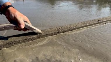 Mason taze beton levhayı geniş bir spatulayla düzleştiriyor. Yakın görünüm.