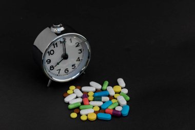 Alarm saati ve siyah arkaplanda çok renkli haplar