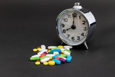 Siyah arka planda alarm saati olan ilaç hapları
