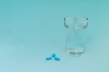 Mavi arka planda bir bardak su olan mavi haplar.