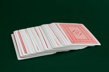 Kırmızı sırtlı, yeşil poker masasında yelpazelenmiş kağıt oynuyor.