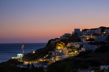 Ios, Yunanistan - 6 Eylül 2022: Nefes kesici mor gün batımı ve Yunanistan 'daki Mylopotas plajındaki aydınlık resimli otel ve restoranların manzarası