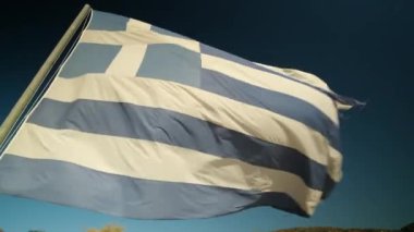 Rüzgarda dalgalanan büyük Yunan bayrağı ve arka planda mavi bir gökyüzü