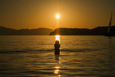 Yunanistan 'daki Mylopotas plajında gün batımını seyreden bir kadın silueti.