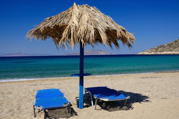 Two sun beds and a sun umbrella at the amazing beach of Agia Theodoti in Ios Greece