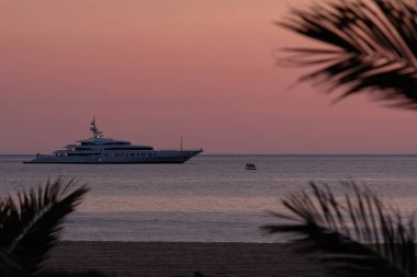 Ios, Yunanistan - 3 Haziran 2021: Güneş dramatik ve renkli bir şekilde batarken, Yunanistan 'ın ünlü Mylopotas plajında lüks bir Yat manzarası