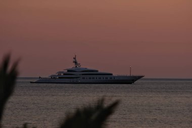 Ios, Yunanistan - 3 Haziran 2021: Güneş dramatik ve renkli bir şekilde batarken, Yunanistan 'ın ünlü Mylopotas plajında lüks bir Yat manzarası