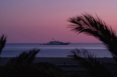 Ios, Yunanistan - 3 Haziran 2021: Güneş dramatik ve renkli bir şekilde batarken, Yunanistan 'ın ünlü Mylopotas plajında lüks bir Yat manzarası