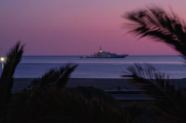 Ios, Yunanistan - 3 Haziran 2021: Güneş dramatik ve renkli bir şekilde batarken, Yunanistan 'ın ünlü Mylopotas plajında lüks bir Yat manzarası