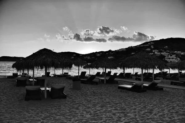 View of empty sun beds and a beautiful sunset at the beach of Mylopotas in Ios Greece in black and white