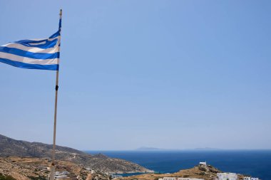 Yunanistan 'ın Ios köyünün tepesinde ve arka planda Ege Denizi' nde dalgalanan Yunan ulusal bayrağının görüntüsü