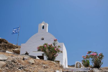 Ios Yunanistan 'daki tepenin tepesinde beyaz boyalı küçük bir kilise ve Yunan ulusal bayrağının manzarası 