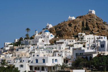 Yunanistan 'ın Ios kentindeki Ege Denizi' ne bakan bir tepenin üzerindeki kilise, küçük şapeller ve Yunan bayrağının panoramik görüntüsü