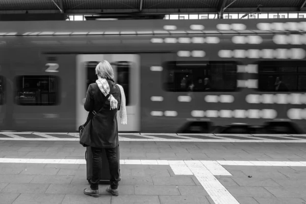 View of a single woman standing at the central rail station of Bonn Germany and a train leaving the platform in black and white