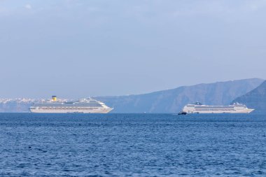 Santorini, Yunanistan - 7 Eylül 2023: Santorini 'nin nefes kesici volkanik manzarasının yanındaki iki büyük yolcu gemisinin görüntüsü