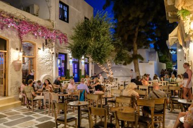 Ios, Yunanistan - 9 Eylül 2023: Barlarla çevrili turistler, gece vakti Yunanistan 'daki popüler meydanda içki ve kokteyllerin keyfini çıkarıyorlar