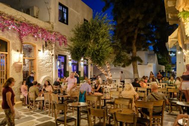 Ios, Yunanistan - 9 Eylül 2023: Barlarla çevrili turistler, gece vakti Yunanistan 'daki popüler meydanda içki ve kokteyllerin keyfini çıkarıyorlar