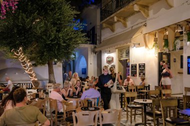 Ios, Yunanistan - 9 Eylül 2023: Barlarla çevrili turistler, gece vakti Yunanistan 'daki popüler meydanda içki ve kokteyllerin keyfini çıkarıyorlar