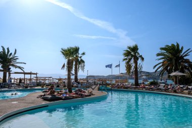 Ios, Yunanistan - 9 Eylül 2023: Genç turistler Yunanistan 'daki ünlü Mylopotas plajı önünde açık havuzun keyfini çıkarıyorlar