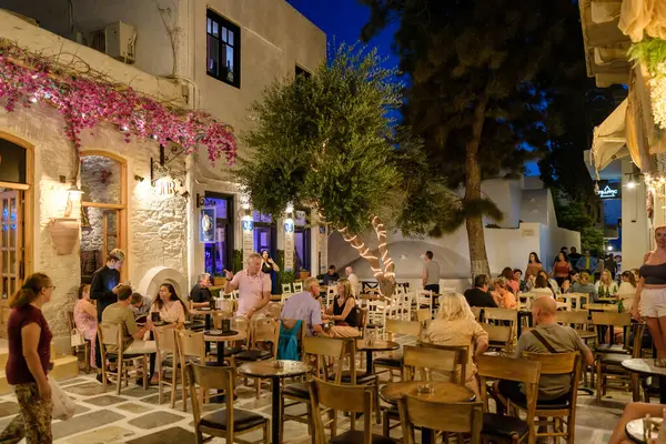 Ios, Yunanistan - 9 Eylül 2023: Barlarla çevrili turistler, gece vakti Yunanistan 'daki popüler meydanda içki ve kokteyllerin keyfini çıkarıyorlar