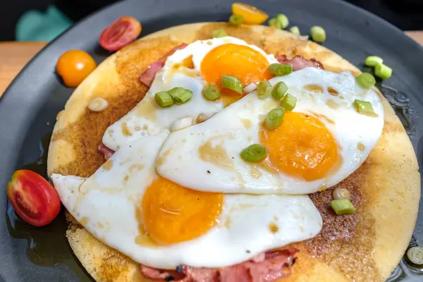 View of fried eggs and bacon on a pancake garnished with tomatoes and onions  in Ios Greece
