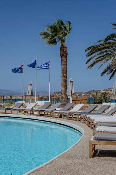 Ios, Yunanistan - 2 Mayıs 2024: Palmiye ağaçları, güneş yatakları ve Ios Yunanistan 'daki ulusal bayraklar ve Avrupa toplumunun yer aldığı güzel bir açık yüzme havuzu manzarası