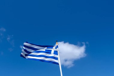 Gökyüzünde sallanan tek bir bulutun ve arka planda mavi bir gökyüzünün yanındaki Yunan bayrağının görüntüsü