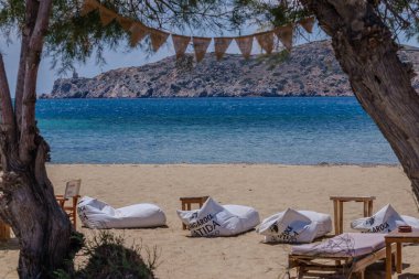 Ios, Yunanistan - 5 Mayıs 2024: Yunanistan 'ın Gialos Plajı' ndaki ağaçların yanındaki plaj barları, masalar ve sandalyeler