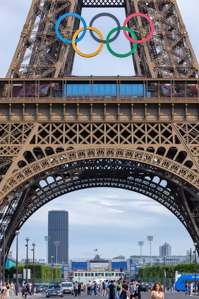 Paris, Fransa - 5 Temmuz 2024: Paris 'teki Olimpiyat yüzükleriyle süslenmiş görkemli Eyfel Kulesi' nin altında yürüyen turistlerin panoramik manzarası