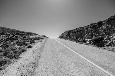 Yunanistan 'da kayalık tepelerin yanındaki boş ve yalnız bir yol manzarası siyah beyaz