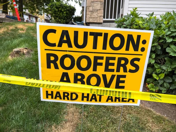 Close up view of a hard hat area sign with caution tape outside of a roof construction zone