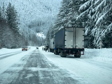 Stevens Pass, WA USA - circa December 2022: Wide view of vehicles putting on snow tire chains on the side of the road during snowy conditions.