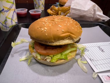 Close up view of a juicy cheeseburger on a fast food tray on a black table indoors