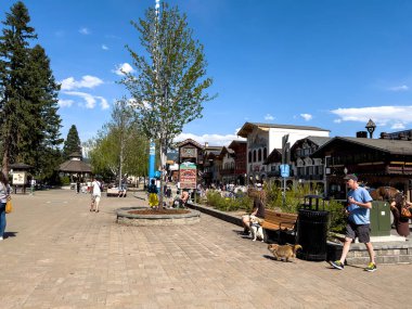 Leavenworth, WA USA - Nisan 2023: Şehir merkezindeki alışveriş bölgesinde güneşli havanın tadını çıkaran insanlar ve köpekler.