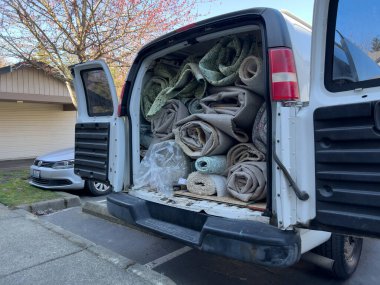 Bothell, WA USA - 5 Kasım 2024: Beyaz bir minibüsün içindeki eski halı rulolarının ve çeşitli diğer halıların görüntüsü.