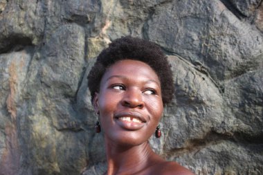 Afro saçlı ve küpeli genç bir Afrikalı kadının çekici bir fotoğrafı. Kayalara karşı güveni tam.
