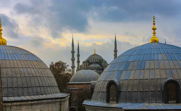 Güneş batarken Mavi Cami kubbesinin manzarası, İstanbul 'un mimari güzelliğini ve dingin atmosferini yansıtıyor. Altın kubbeler ve minareler dramatik gökyüzüne karşı şehrin zengin kültürel mirasına bir göz atmak için duruyorlar..