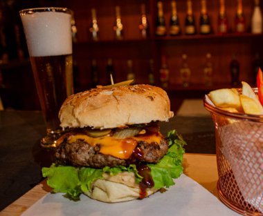 Peynirli, marullu ve soslu lezzetli görünümlü bir hamburger. Yanında da soğuk bir bira. Bu iştah açıcı düzen, rahat bir ortamda lezzetli bir yemek sergilemek için mükemmel..
