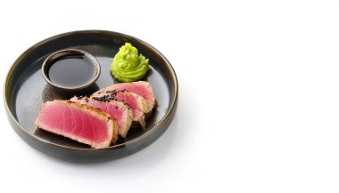 crusted seared raw Ahi Tuna Steaks - aka known as yellowfin or bigeye tuna fish - Thunnus albacares - with green wasabi and soy sauce isolated on white background with copy space. A popular appetizer clipart