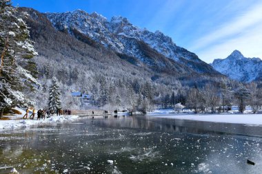 Julian 'daki dağlar Slovenya' daki Kranjska Gora yakınlarında Jasna Gölü 'nün yukarısındaki dağlarda insanlar kıyıda yürüyor.