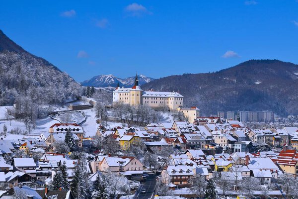 View of Skofja Loka castle and the town bellow in Gorenjska, Slovenia in winter and forest covered hills in the background