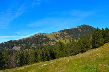 Veliki Zvoh mountain at Krvavec with the hotel and the antenna bellow and a conifer forest covering the hill bellow in Gorenjska, Slovenia clipart